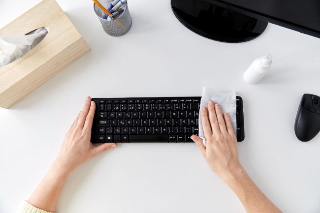 A person wiping down their keyboard with cleaning wipes