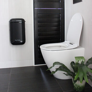 A black Pod Petite sanitary disposal unit beside toilet with a Pod Wrap Carbon Fibre decal.