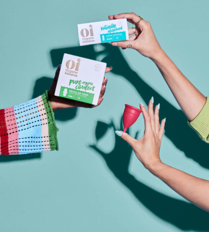 A range of period products being held with womens hands with a mint green background