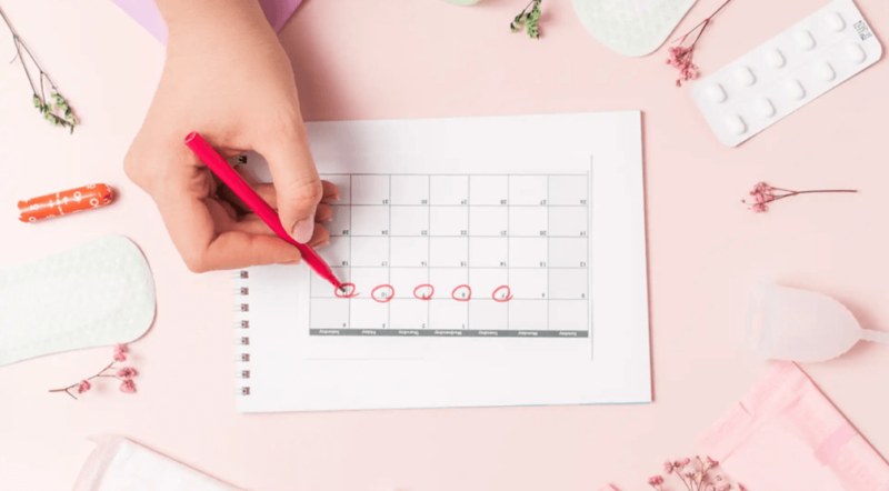 Feminine hygiene tips - a woman's hand marking her period on a calendar, pink background with feminine products and flowers around.