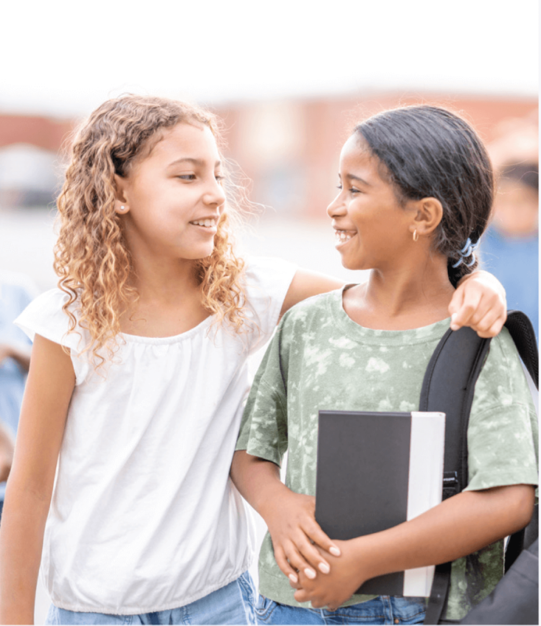 Girls at school smiling with their arms around each other, carrying backpacks and books